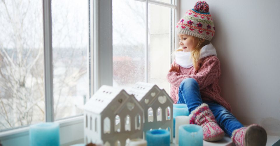 Girl inside dressed in hat and scarf looking out window